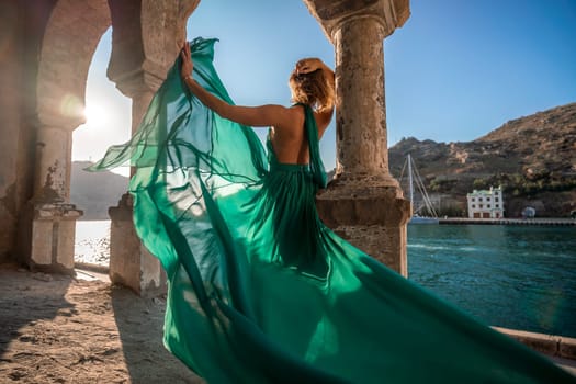 Woman dress sea columns. Rear view of a happy blonde woman in a long mint dress posing against the backdrop of the sea in an old building with columns