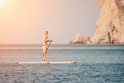 Sea woman sup. Silhouette of happy middle aged woman in rainbow bikini, surfing on SUP board, confident paddling through water surface. Idyllic sunset. Active lifestyle at sea or river