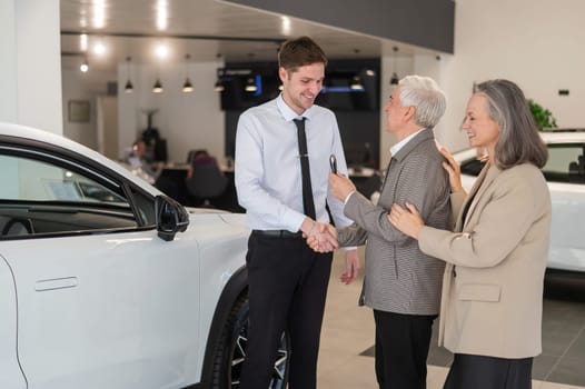 A salesman hands over the keys to a new car to an elderly Caucasian couple