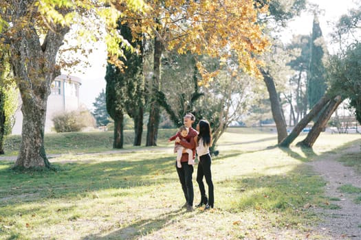 Mom hugs a laughing dad with a little girl in his arms in an autumn park. High quality photo