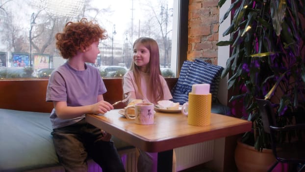 Boy and girl are talking in cafe. Stock footage. Cute couple of kids are sitting in cafe. Children chat sweetly together in cafe. Childhood infatuation.