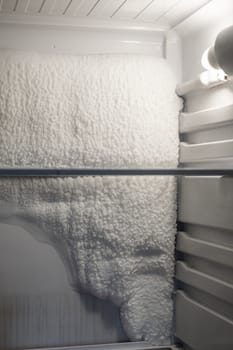 Frozen refrigerator that needs to be defrosted. Block of ice in the empty fridge. empty shelves in the refrigerator. Refrigerator maintenance.