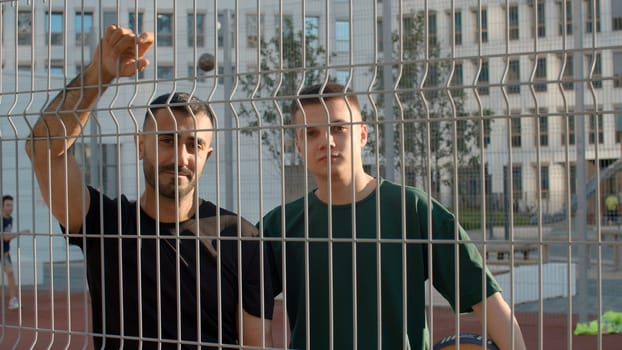 Athletic men. Media. Two friends standing in an embrace behind a special net and preparing to play volleyball with a sports ball. High quality 4k footage
