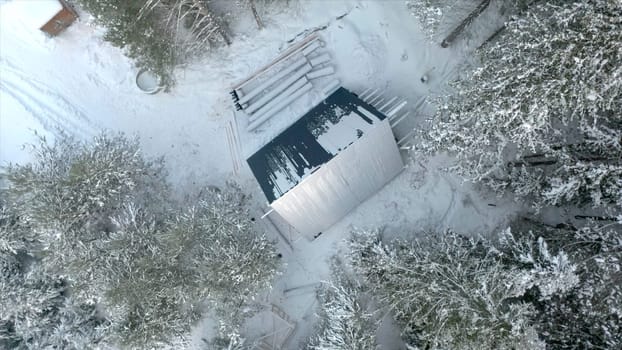 Top view of construction site of house in forest in winter. Clip. House under construction in dense coniferous forest in winter. Construction of single house in wilderness in winter.