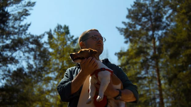 Positive young man holding his beloved dog Jack Russell Terrier and is enjoying a sunny summer day. Stock footage. The concept of love for pets