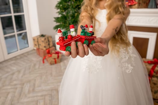 Hands of a child holding a gift, A wooden train toy is carrying New Year's gifts. On a cozy knitted gray sweater. top view.