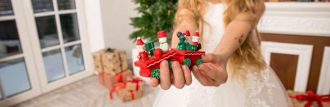 Hands of a child holding a gift, A wooden train toy is carrying New Year's gifts. On a cozy knitted gray sweater. top view.