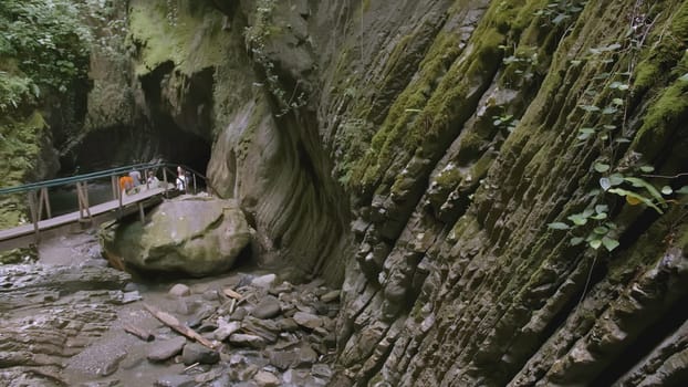 A group of tourists walks in the mountains. CREATIVE. Several teenagers with their parents decided to take a walk in the caves in the stone walls. People walk on hanging bridges along stone cliffs.