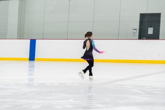 Young girl perfecting her figure skating routine while wearing her competition dress at an indoor ice rink.