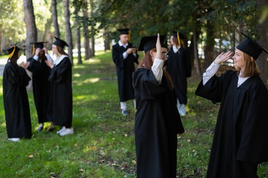 A group of graduates in robes congratulate each other on their graduation outdoors
