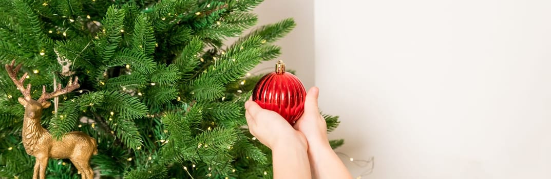 winter holidays and people concept - close up of young woman hand decorating christmas tree with red ball over snow