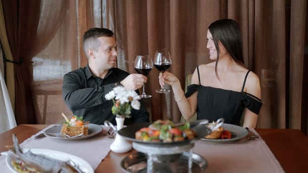 Young beautiful couple having a dinner in a restaurant. Action. Elegant man and woman couple on a date sitting at a table with dishes and wine