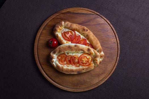 top view of Adjarian khachapuri with tomatoes on a wooden stand.