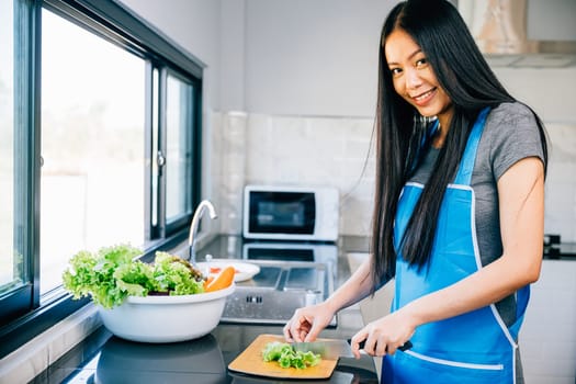A smiling woman in an apron cuts fresh vegetables for a healthy salad illustrating home cooking. Close-up of a cheerful housewife preparing a nutritious dinner.