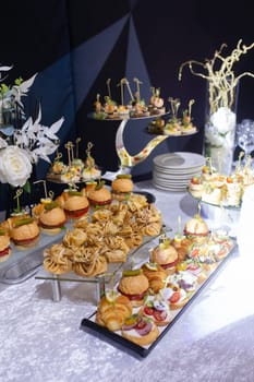 Croissants, burgers and various snacks on stands on the buffet table.