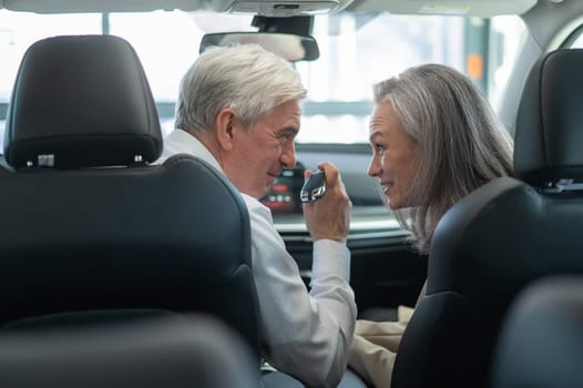 Mature Caucasian couple sitting in a new car and rejoicing at the purchase