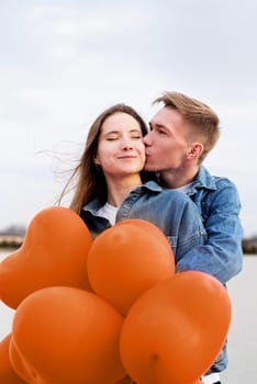 Color of the year 2024: Peach Fuzz. Valentines Day. Young loving couple hugging and holding heart shaped balloons outdoors