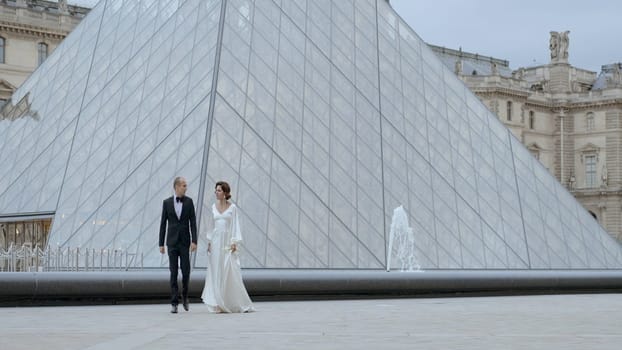 Wedding couple walking on the background of the Louvre pyramid, France, Paris. Action. Romantic wedding shooting near museum