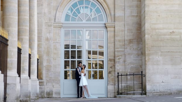 A gentle couple at a photo shoot in the summer. Action. A bright young couple with a girl in a short white dress and a man in a suit who pose on the street next to buildings. High quality 4k footage