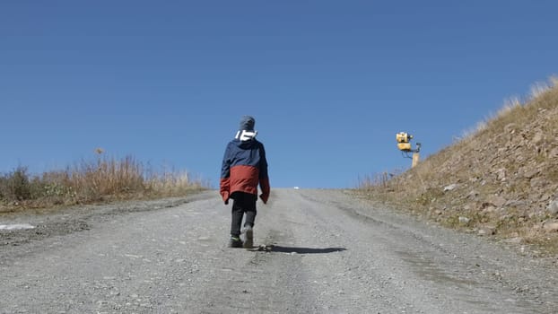 Boy goes up mountain road. Creative. Boy is walking on road uphill. Boy climbs mountains on road on autumn sunny day.