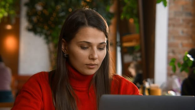 Beautiful woman is typing on laptop in cafe. Stock footage. Attractive young woman is working at laptop in cafe. Beautiful woman is typing on laptop while freelancing in cafe.