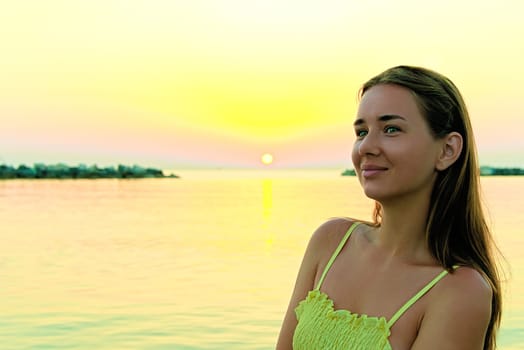 Close-up portrait of a young woman in a yellow dress at sunrise against the background of the sea. Woman walks on the seashore