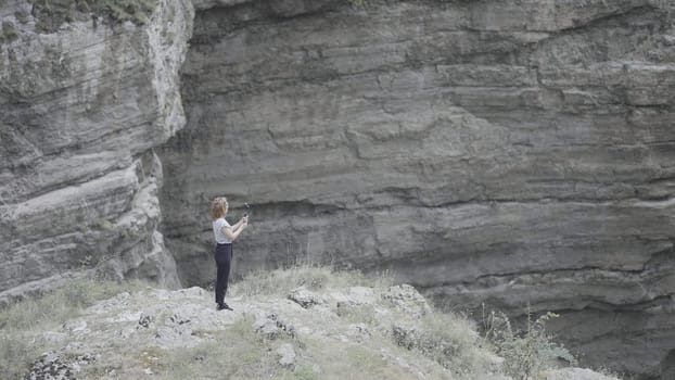 Woman takes pictures on phone with steadicam of mountain. Action. Beautiful woman in the mountains among rocks takes pictures on phone. Woman professionally shoots rock landscapes and waterfalls on phone.