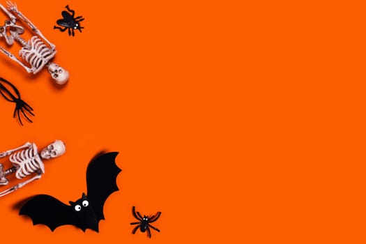 Halloween decoration flat lay - orange background with spiders, bat, skeletons. Place for your text.