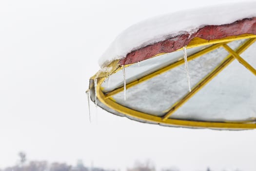 This image features a snow-covered umbrella with icicles hanging, against a blurred winter landscape