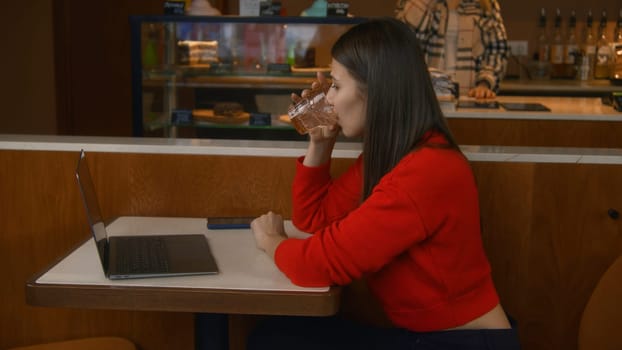 Beautiful woman is seriously working at laptop in cafe. Stock footage. Attractive young woman is working thoughtfully at laptop. Woman works with clients on freelance basis from laptop in cafe.