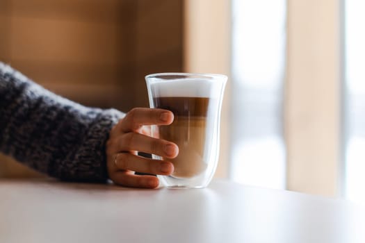 Woman's hand in gray sweater puts milk foam in cappuccino.