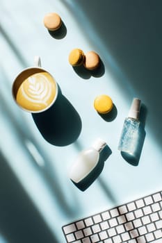 Flat lay with tasty cappuccino and macaroons in sunlights hand sanitizer or cream, liquid eye patches. Face and body care while working at the computer.