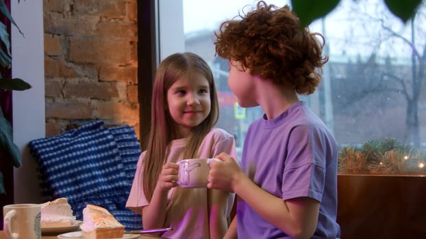 Cute happy children holding together one cup of hot sweet drink. Stock footage. Boy and girl, sister and brother at a cafe