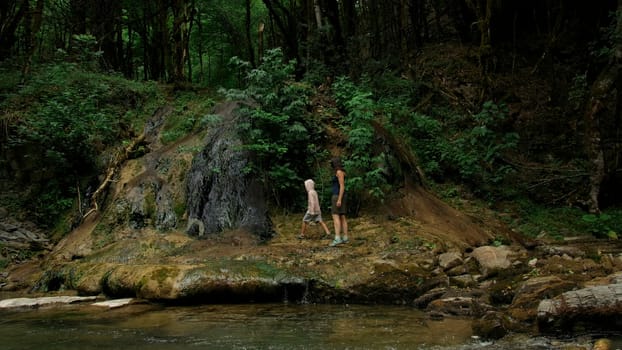 Mother and boy walking along the river and giant stones. Creative. Green dense forest on the background