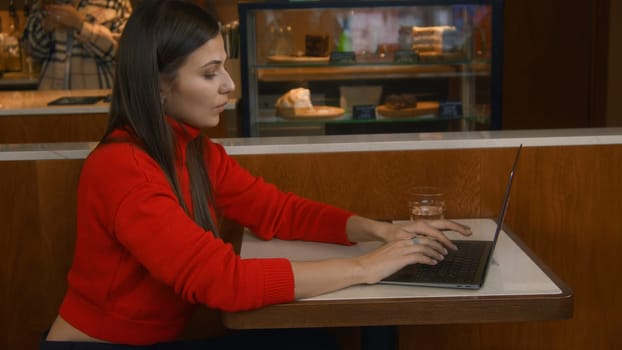 Beautiful young woman working at laptop in cafe. Stock footage. Beautiful woman is puzzled working with laptop in cafe. Woman freelancing at laptop in cafeteria.