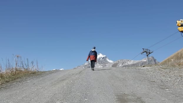 Boy goes up mountain road. Creative. Boy is walking on road uphill. Boy climbs mountains on road on autumn sunny day.