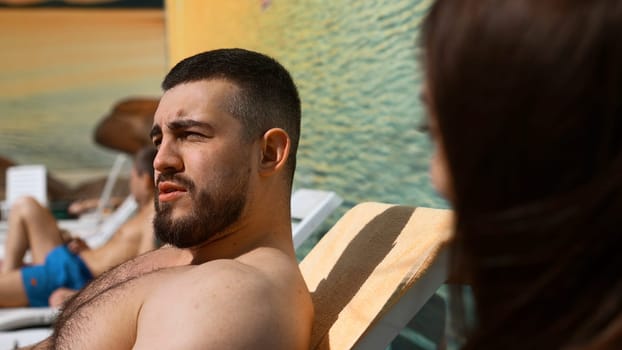 Young couple in a hotel relaxing on sunbeds and communicating. Clip. Brunette man and woman flirting with each other at the vacation