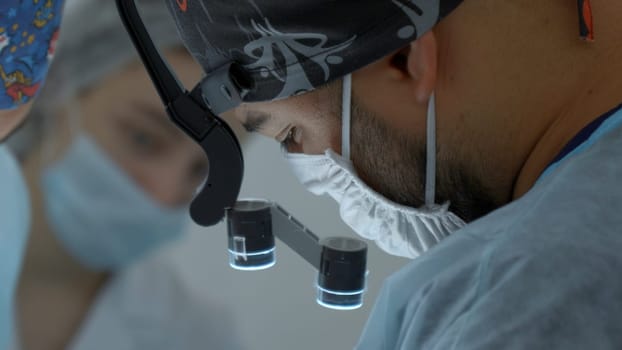 Surgeon head with professional glasses at operating room. Action. Close up side view of a doctor in glasses with binocular magnifiers