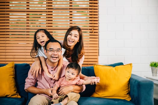 In their modern home a happy family enjoys a sweet moment on a comfortable sofa. Parents daughters and siblings share quality time smiling and embracing showcasing family togetherness.