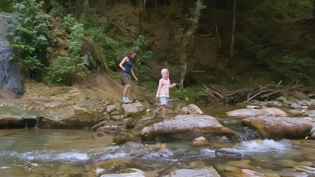 Woman and boy walk by river in forest. Creative. Mother and child walk in wild forest with river in summer. Family trip to wild forest in summer.