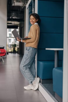 Pretty female freelancer working on laptop while standing on modern coworking background