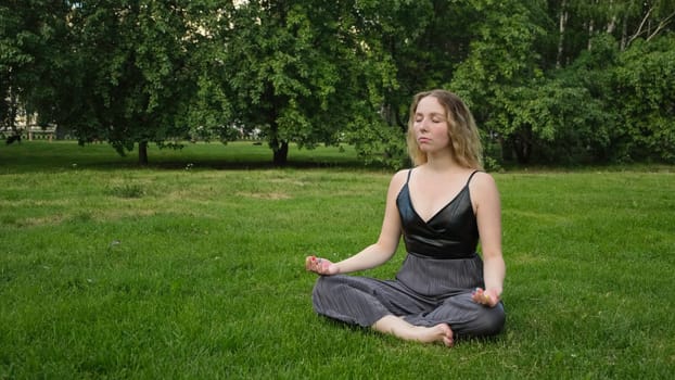 Young beautiful woman doing yoga in park. Concept. Young woman does yoga on green grass in park. Woman meditates and does yoga in city green park.