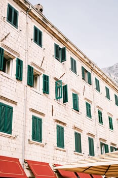 Stone facade of an ancient apartment building with green shutters on the windows. High quality photo