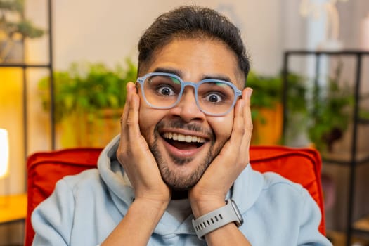 Oh my God Wow. Excited amazed young Indian man surprised looking at camera with big eyes shocked by sudden victory good win news celebrating success triumph. Portrait of happy Arabian guy at home room
