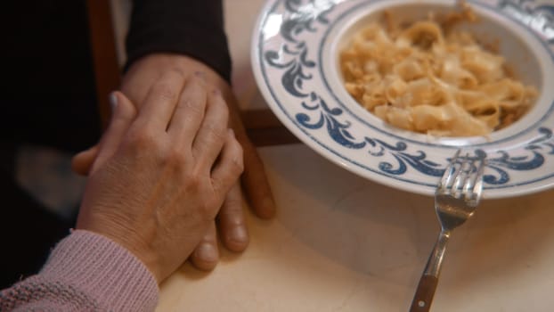 Hands of elderly couple on table. Stock footage. Gentle touches of hands of elderly couple in love. Hands of elderly couple on table with plate of pasta for romantic dinner.