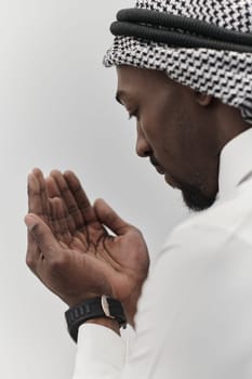 African American Muslim man raises his hands in prayer, seeking solace and devotion to God, as he stands isolated against a serene white backdrop, symbolizing a profound expression of faith and contemplation.