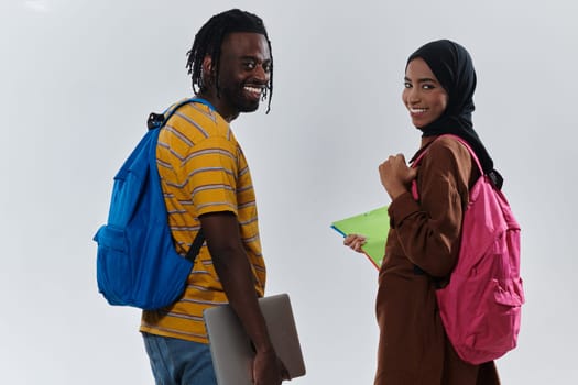 African American student collaborates with his Muslim colleague, who diligently works on her laptop, symbolizing a blend of diversity, modern learning, and cooperative spirit against a serene white background.