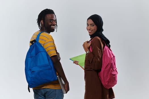 African American student collaborates with his Muslim colleague, who diligently works on her laptop, symbolizing a blend of diversity, modern learning, and cooperative spirit against a serene white background.