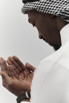 African American Muslim man raises his hands in prayer, seeking solace and devotion to God, as he stands isolated against a serene white backdrop, symbolizing a profound expression of faith and contemplation.