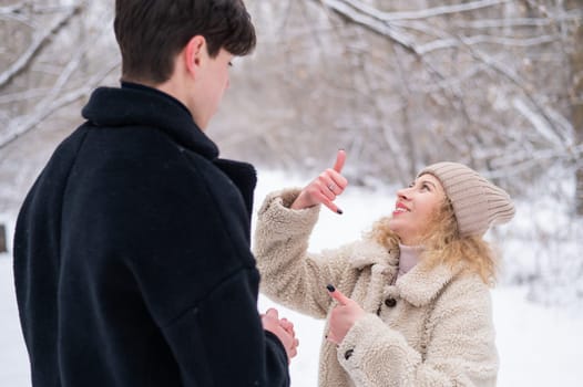 A young couple walks in the winter in the forest. Deaf Guy and a girl communicate using gestures outdoors